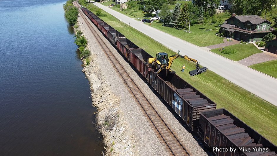 On June 2, 2021, the work train showed up with the tie distribution crew. That’s a fairly standard backhoe with tricked-out outriggers and a bracket on the front bucket to allow it to rest (and be moved upon) the top chords of the tie hoppers. The excavator is equipped with a grapple instead of the typical digging bucket.