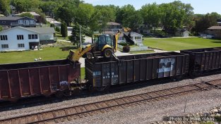 On June 2, 2021, the work train showed up with the tie distribution crew. That’s a fairly standard backhoe with tricked-out outriggers and a bracket on the front bucket to allow it to rest (and be moved upon) the top chords of the tie hoppers. The excavator is equipped with a grapple instead of the typical digging bucket.